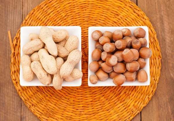 Amendoins e avelãs em uma tigela branca em um guardanapo de vime — Fotografia de Stock