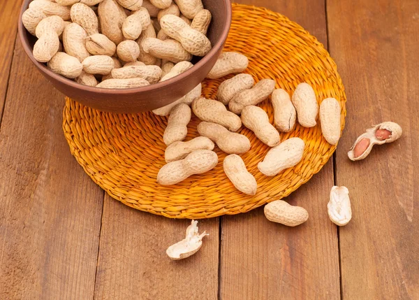 Peanuts in a clay bowl on a wicker orange place mat — Stock Photo, Image