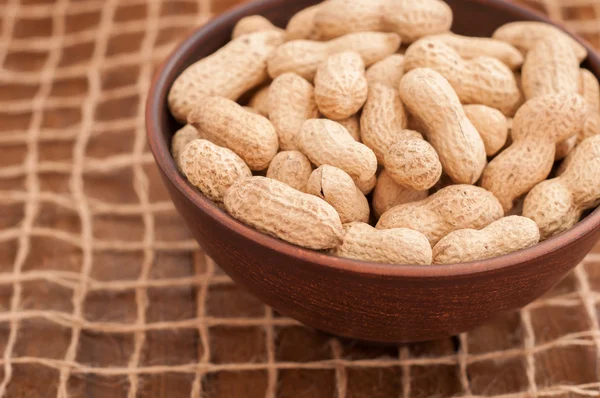 A bowl of peanuts on a grid of twine. Wooden brown background — Stock Photo, Image