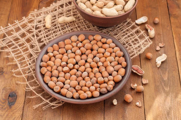 Avellanas y cacahuetes en cuencos de barro sobre fondo de madera — Foto de Stock