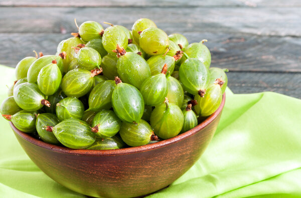 Fresh green gooseberries in a ceramic bowl on textile napkin. Go