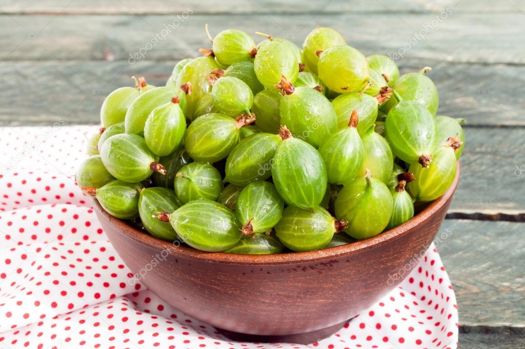 Fresh green gooseberries in a ceramic bowl on a napkin textile. 