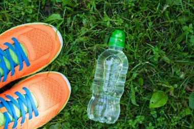 Spor ayakkabıları ve taze yeşil çimlerin üzerinde bir şişe su.