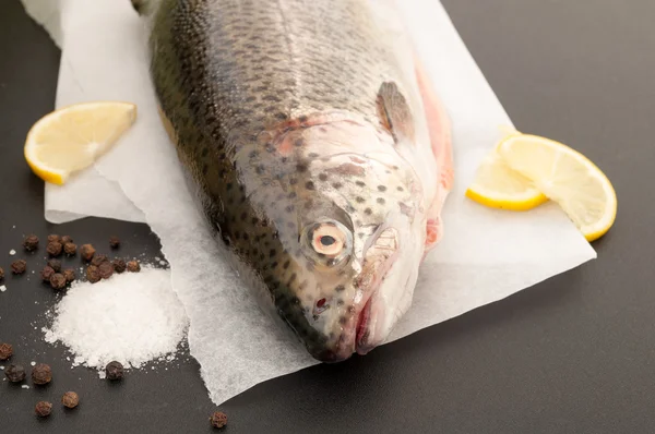 Forellenfisch mit Zitrone, Salz und schwarzem Pfeffer auf schwarzem Backblech — Stockfoto