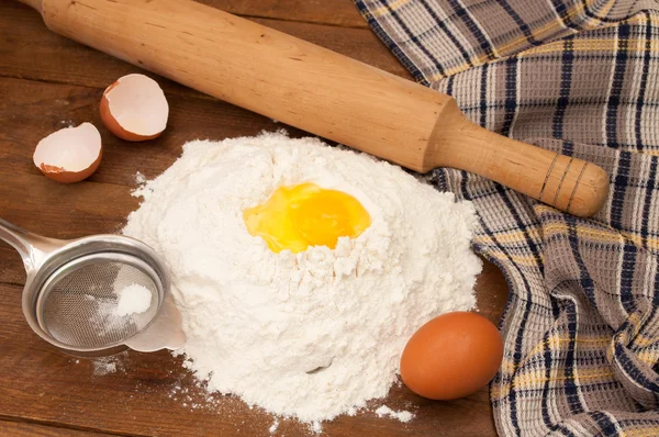 Baking ingredients: eggs and flour, sieve and rolling pin on woo — Stock Photo, Image