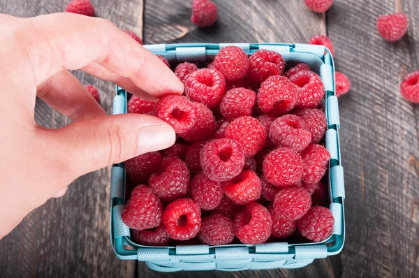 Frische Himbeeren im Korb auf Holzuntergrund. Hand nimmt — Stockfoto