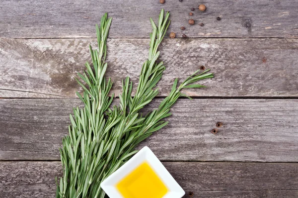 Rosemary, olive oil and pepper on old wooden background — Stock Photo, Image