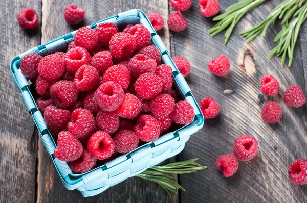 Verse frambozen in een mand en rozemarijn op een houten pagina — Stockfoto