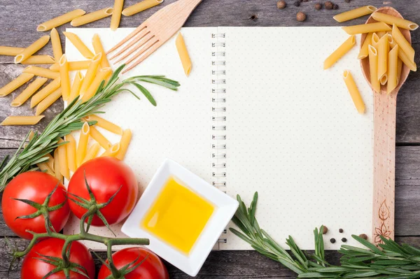 Open cookbook, spoon with penne pasta, tomatoes, rosemary and ol — Stock Photo, Image