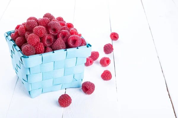 Verse frambozen in een rieten mand op een witte houten pagina — Stockfoto