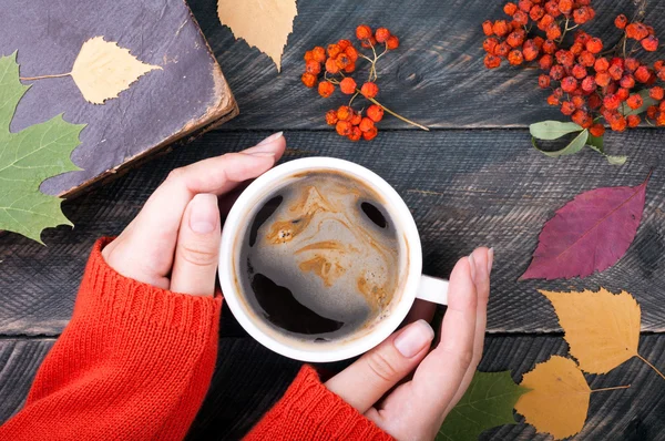 Manos de mujer sosteniendo taza de café sobre fondo de madera de otoño. O — Foto de Stock