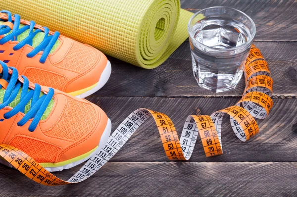 Sportschoenen, yoga mat, glas water en centimeter op houten — Stockfoto