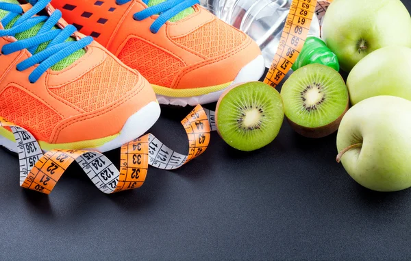 Sport shoes, fruits,  bottle of water and measuring tape on dark — Stock fotografie