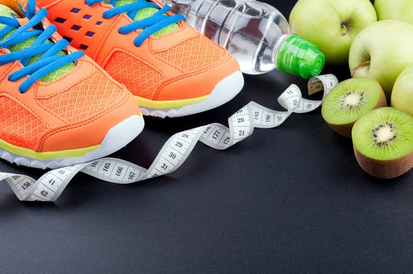 Sport shoes, fruits,  bottle of water and measuring tape on dark — Stockfoto