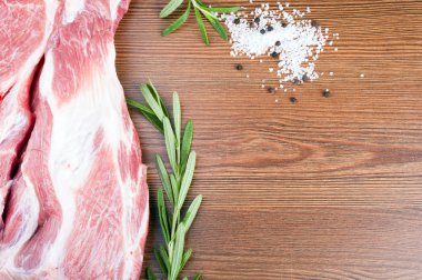 Raw meat, rosemary and salt on wooden background