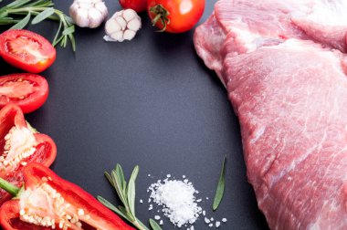 Raw meat pork with pepper, tomatoes, rosemary and garlic on a da