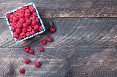 Raspberries in a basket on old wooden background. Rustic style