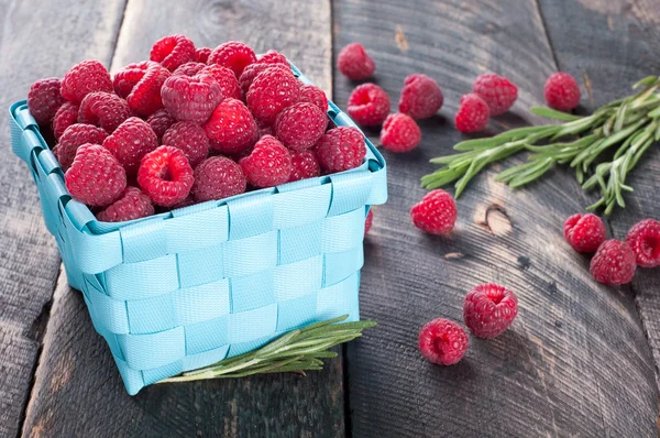 Fresh raspberries in a basket and rosemary on a wooden backgroun — Stock Photo, Image