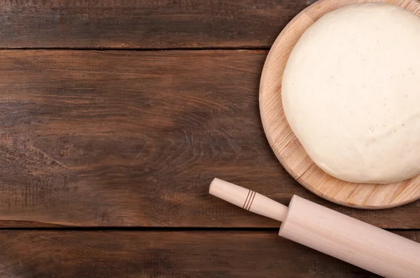 Ball of dough for pizza and rolling pin on old wooden background