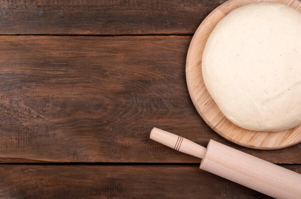 Ball of dough for pizza and rolling pin on old wooden background