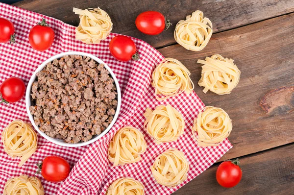 Minced meat, tagliatelle and cherry tomatoes on a wooden table. — Stock Photo, Image