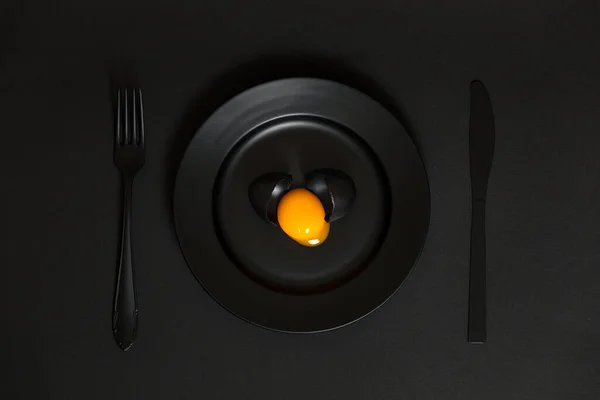 Huevo Negro Roto Con Yema Amarilla Plato Con Cuchillo Tenedor Imagen De Stock