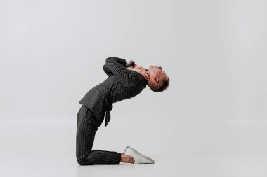 Yan görüş. Smokinli bir adam dizlerinin üstünde kendine sarılıyor..