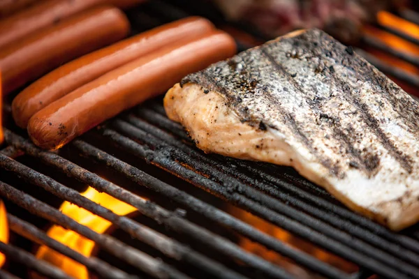 Hotdogs, steaks en zalm op een grill — Stockfoto