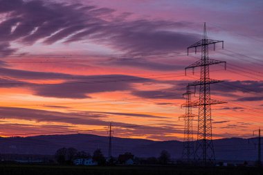 Parlak bulut oluşumları ve elektrik direklerinin hatlarıyla renkli ve yüksek kontrastlı bir gündoğumu görüntüsü