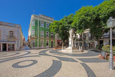 Colorful mosaic square with green tiled house trees and cafes in Loule Algarve Portugal under a clear blue sky