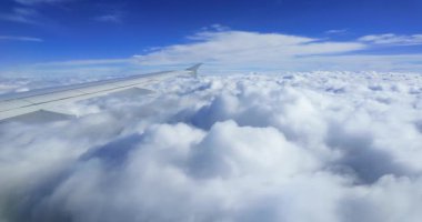 Derin mavi bir gökyüzünün altında kapalı beyaz bulut tabakasının üzerinde uçan bir yolcu uçağının hava görüntüsü. Huzurlu ve huzurlu atmosfer hava yolculuğunun güzelliğini ve doğanın enginliğini gösteriyor.