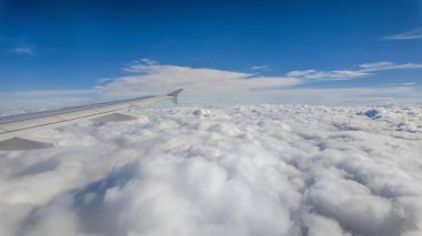 Derin mavi bir gökyüzünün altında kapalı beyaz bulut tabakasının üzerinde uçan bir yolcu uçağının hava görüntüsü. Huzurlu ve huzurlu atmosfer hava yolculuğunun güzelliğini ve doğanın enginliğini gösteriyor.
