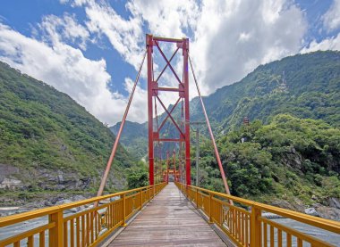 Tayvan 'da asma bir köprüde ahşap bir yürüyüş yolu. Bereketli dağlar sarp arazi ve parlak gökyüzü manzaralı bir manzara oluşturuyor..