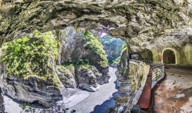 Tayvan 'daki Taroko Boğazı' nın panoramik manzarası uçurum kenarındaki tünelleri, dik kaya duvarlarını ve aşağıda dönen gri bir nehri gösteriyor..