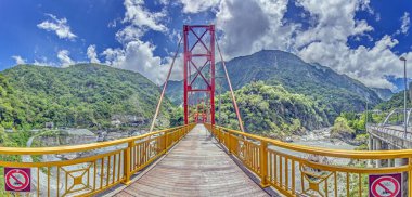 Tayvan 'da asma bir köprüde ahşap bir yürüyüş yolu. Bereketli dağlar sarp arazi ve parlak gökyüzü manzaralı bir manzara oluşturuyor..