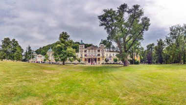 Marianske Lazne 'nin şık spa kompleksinin geniş panoramik manzarası. Parktaki çimlerle çevrili ve yazın bulutlu gökyüzü..