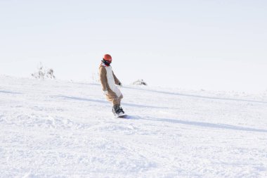 Kar altında dağları olan bir snowboard 'a binerken, ceketli genç bir adam büyük bir hızla kar üzerinde hareket eder.