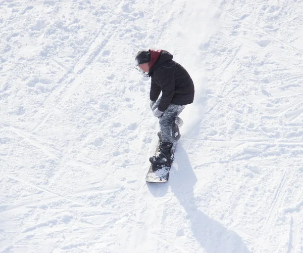 雪の中で山と一緒にスノーボードに乗っていると ジャケットの若い男がボード上の雪の上に素晴らしいスピードで動きます — ストック写真