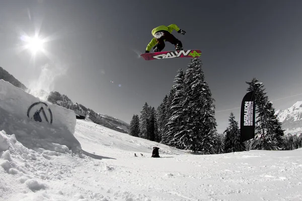 Ein Mann fliegt durch die Luft, während er mit einem Snowboard einen schneebedeckten Hügel hinunterfährt — Stockfoto
