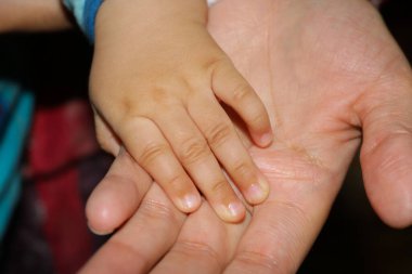 Küçük bebek annesinin elini tutuyor.