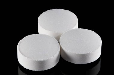 Birbirlerine tıpatıp benzeyen üç beyaz ilaç tabletinin yakın çekim stüdyosu. Hafif desenli yüzeyi var. Karanlık bir boşluğa karşı izole edilmiş.