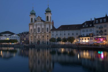 İsviçre 'nin Lucerne kentindeki tarihi Cizvit Kilisesi ve rıhtım binaları alacakaranlıkta güzelce aydınlatılmış ve Reuss Nehri' nde yansımalar parıldıyor.