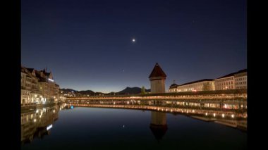 İsviçre 'nin Lucerne kentindeki tarihi Chapel Köprüsü ve Su Kulesi alacakaranlığın yumuşak renklerinde Reuss Nehri' nin sakin sularında güzel bir şekilde yansıtılır.