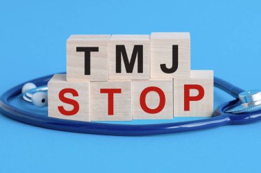 Üzerinde TMJ yazan tahta blok. Masada steteskop, sigorta ve tıbbi konsept, mavi arka plan, sağlık sigortası ve tıbbi konsept ile dur..