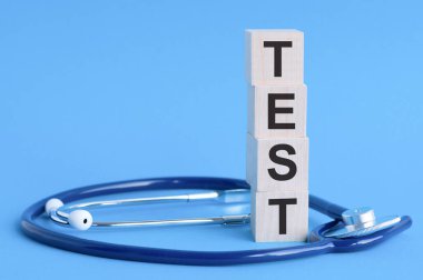 Tahta bloklara ve açık mavi arka planda steteskopa test kelimesi yazıldı. sigorta ve tıbbi konsept