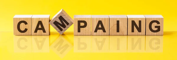 CAMPAING word written on wood block. CAMPAING word is made of wooden building blocks lying on the yellow table. CAMPAING, business concept, yellow background