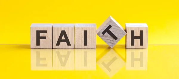 FAITH word written on wood block. FAITH word is made of wooden building blocks lying on the yellow table. FAITH, business concept, yellow background