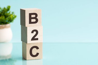 Açık mavi arkaplanlı B2C alfabesinin harfi. Yazılı metin parlak yüzeyden yansıtılır. Arka planda saksıda bir çiçek var. b2c - işletmeden tüketiciye