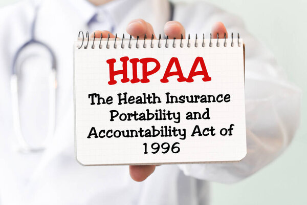 Doctor holding a card with text HIPPA - The Health Insurance Portability and Accountability Act of 1996 - medical concept. The text is written in red letters in a medical journal.