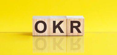 Tahta bloğa yazılmış bir kelime. Sözcük, sarı masanın üzerinde duran ahşap yapı taşlarından oluşur. OKR - Hedefler ve Anahtar Sonuçlar - iş konsepti, sarı arkaplan